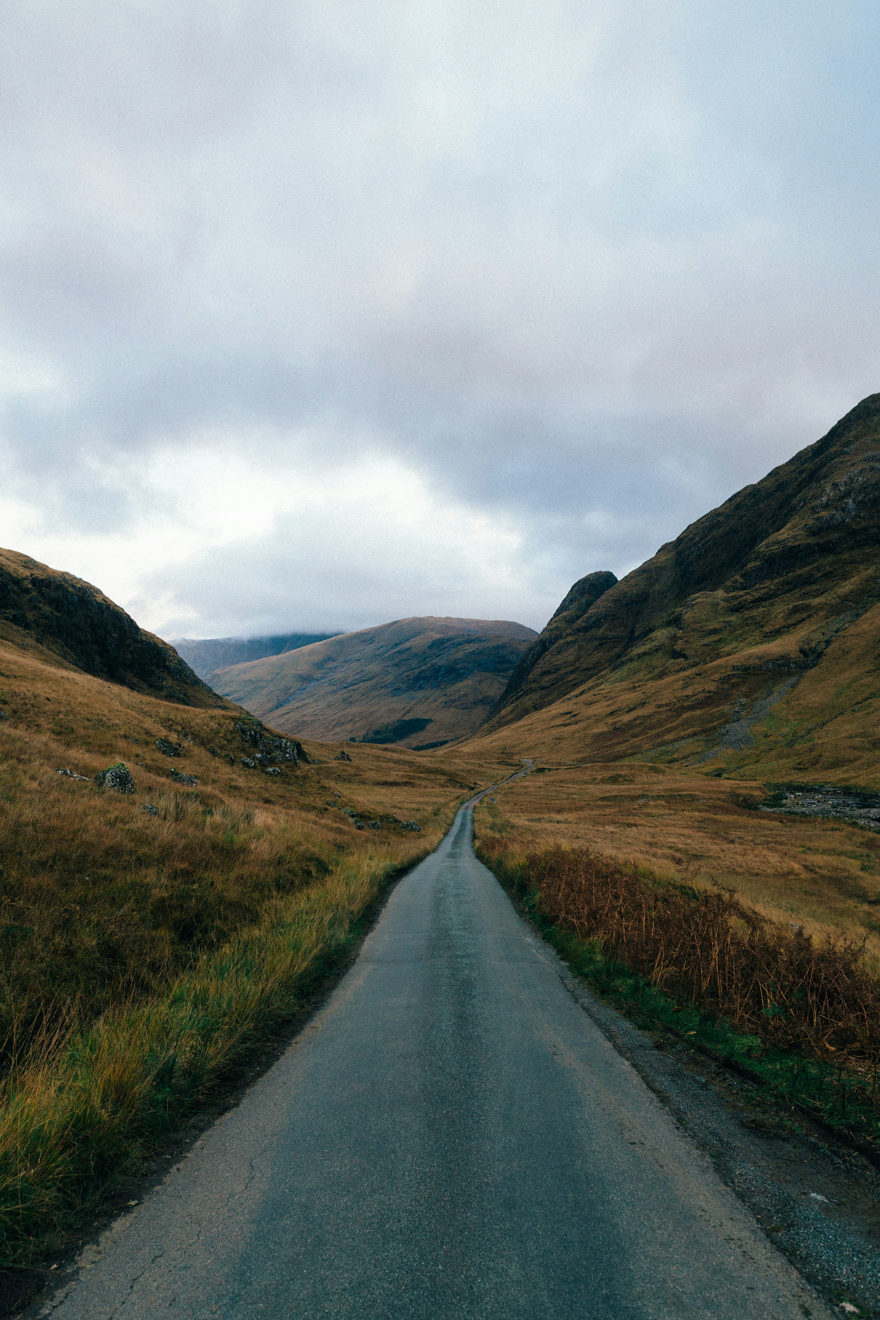 empty road between brown mountains under blue sky